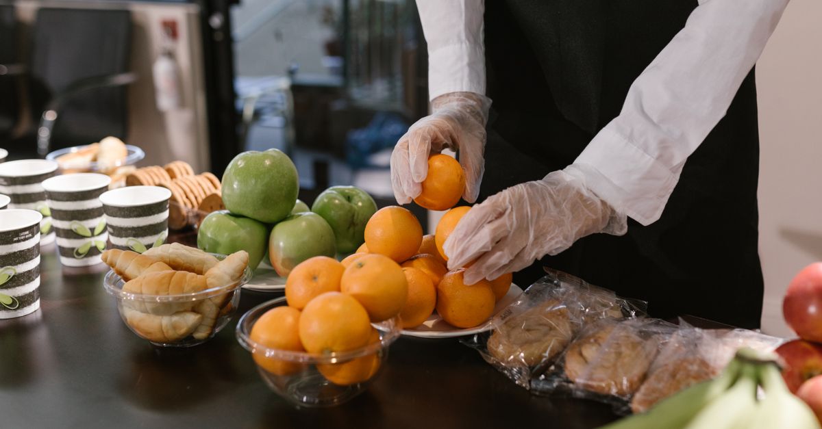 Caterer arranging fresh fruits and snacks on a table for a food service event.